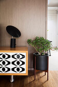 Black lamp on lowboard with black and white front next to plant stand