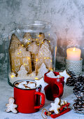 Cocoa in red cups with marshmelow, gingerbread men and gingerbread city in a glass jar in Christmas style