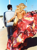 A blonde woman wearing a printed, backless summer dress and a man in a suit