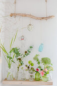 Twigs and flowers in various vases below ornaments hung from branch