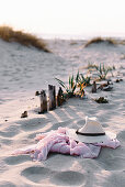 Strohhut und rosa Schal liegen am Strand