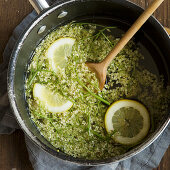 Freshly picked elderflowers in a large saucepan with lemons and a wooden spoon