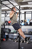 Junger Mann bei Fitnessübung Burpee Jumping Pull-Up an der Klimmzugstange