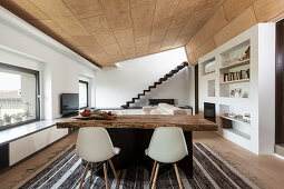 Rustic wooden table, classic chairs and fitted shelves in open-plan interior
