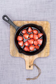 Strawberries baked in sugar on the bbq in a black pan, at a wooden plank at linen