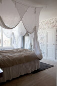 Double bed with white canopy in bedroom with vintage wallpaper