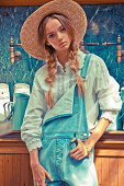 A young woman wearing a straw hat, a light blue blouse with lace trim and dungarees