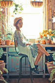 Junge Frau mit Strohhut im Wickelkleid im Gartenhäuschen