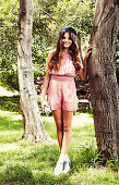 A young, dark-haired woman standing by a tree wearing a jumpsuit