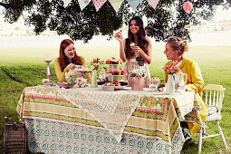 Three young women sitting at a festively laid garden table