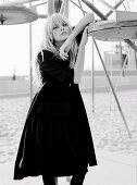 A blonde woman wearing a black coat on a beach (black-and-white shot)