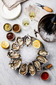 Open Oysters with lemon, sauce and Champagne in ice bucket on white marble background