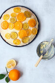 A round orange cake spread with butter icing and decorated with slices of candied lemon, lime and orange