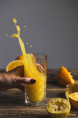 Frauenhand hält Glas mit spritzendem frischgepresstem Orangensaft