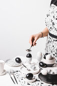 A woman wearing an apron in front of a table laid in black-and-white with coloured eggs