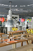 Wooden tables and benches in restaurant; colourful rubber rings above bar in background