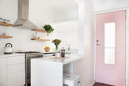 weiße Einbauküche mit Frühstückstheke neben rosa Eingangstür