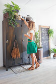 Woman next to vintage metal lockers, houseplants and chalkboard in living room