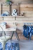 Desk against wooden wall and denim clothing hung from hooks on wall