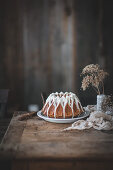A gingerbread bundt cake with vanilla white glaze on a wood table