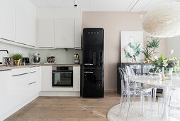L-shaped kitchen counter, black fridge and dining area with designer chairs in bright kitchen
