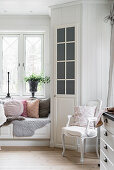 Window seat with scatter cushions next to pantry door in white kitchen-dining room