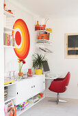 White sideboard below small workspace with screen print and shelves on wall