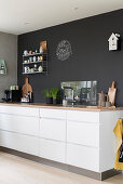 White kitchen counter with drawers and wooden worksurface against charcoal wall