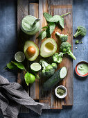Flat lay of arranged greens of fresh broccoli with cucumber and avocado among green herbs on wooden board