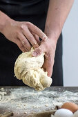 Man in Black Apron Holds Raw Dought in His Hands