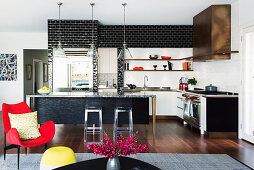 Schwarze und weiße Wandfliesen in offener Küche mit Kücheninsel, im Vordergrund roter Sessel