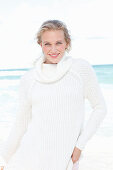 A young blonde woman by the sea wearing a white jumper