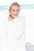 A young blonde woman by the sea wearing a white jumper