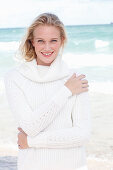 Junge blonde Frau in weißem Pullover am Meer