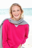 Junge blonde Frau in pinkfarbenem Pullover und grauer Pullover über den Schultern