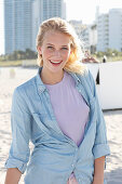 A young blonde woman wearing a purple t-shirt and a denim shirt