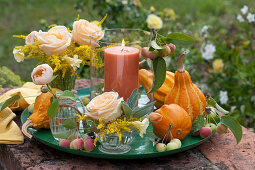 Kleine Sträuße aus Rosen und Goldrute mit Windlicht und Zierkürbissen auf Schale