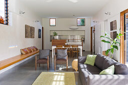Grey sofa, fitted wooden bench, dining table and fitted kitchen in open-plan interior with concrete floor