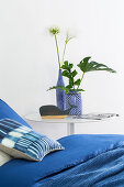 Blue bed linen on bed next to leaves and flowers in blue-and-white vases on bedside table
