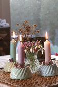 Kerzenständer in Guglhupfform mit brennenden Kerzen und Schneeglöckchen als Tischdeko