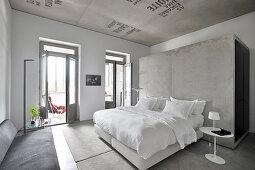 Doppelbett mit weißer Bettwäsche vor Betonwand im Hotelzimmer