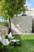 Classic chairs and side table on lawn in garden with terrace in background