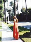 A young brunette woman wearing a long, orange summer dress