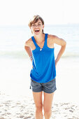 A mature brunette woman on a beach wearing a blue top and a silver bracelet