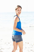 A mature brunette woman on a beach wearing a blue top and a silver bracelet