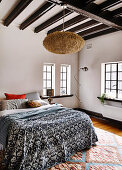 Doppelbett mit Tagesdecke, darüber marokkanische Lampe im Schlafzimmer mit dunklen Deckenbalken