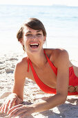 A mature brunette woman on a beach wearing a red bathing suit