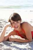 A mature brunette woman on a beach wearing a red bathing suit