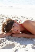 A mature brunette woman on a beach wearing a red bathing suit