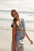 A mature blonde woman on a beach wearing a silver summer dress